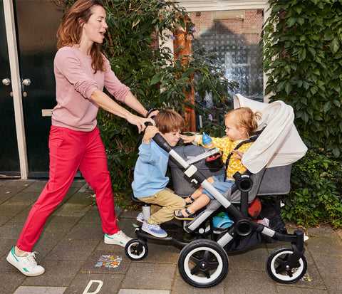 Woman pushing three children in Bugaboo Donkey3 Duo. One child is on the bugaboo wheeled board