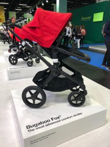 Side view of the Bugaboo Fox2 stroller; it has a red canopy and sits in a showroom atop a white platform that reads "Bugaboo Fox2".