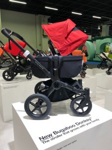 Bugaboo Donkey3 stroller with a red canopy sits atop a white platform in a showroom; the platform reads "New Bugaboo Donkey3"