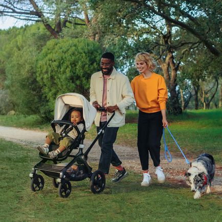 happy couple walk their baby in a bugaboo fox 3 stroller with their dog in a green park