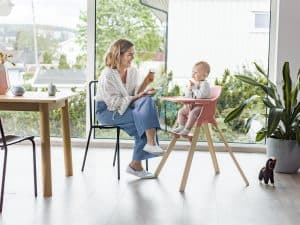 Child and mother sitting next to a kitchen table, with the child sitting in a pink Stokke Clikk Clakk high chair.