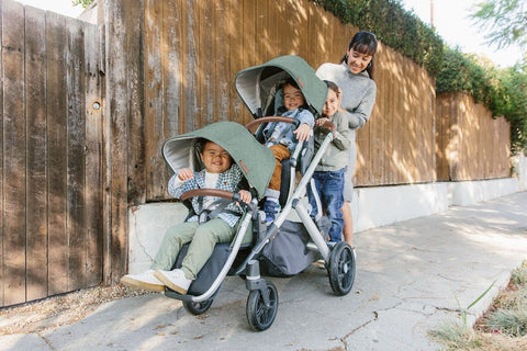 Woman pushing three kids in UPPAbaby Vista V2 with piggyback ride along board 