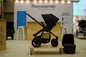 Black Bumbleride Era stroller on top of a wooden platform with a sign reading "Bumbleride" in the background.