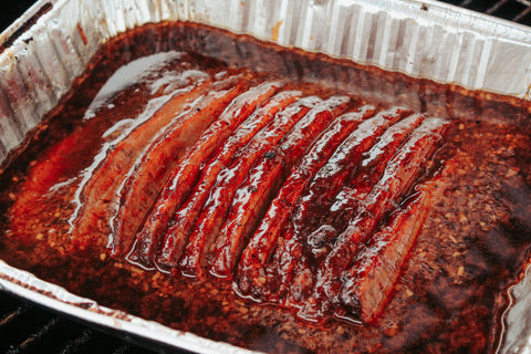 Sliced brisket sitting in a tray of sauce