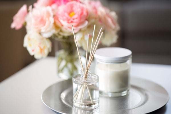Scented candle and diffuser on coffee table with flowers in the background