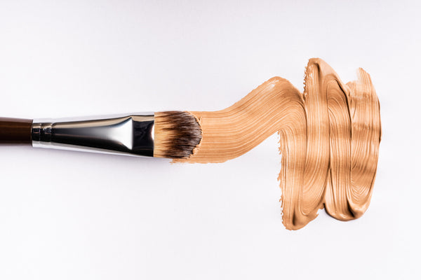 Flat makeup brush with liquid foundation texture swatch on white background