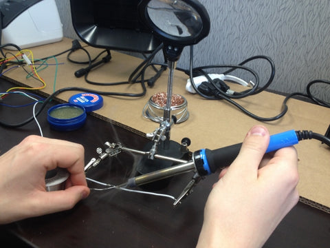 Photo of arm's of a man holding soldering iron and around tools necessary for solder