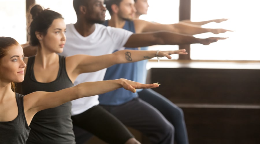 Gruppe von Menschen in einem Yogastudio in der Krieger-Yoga-Pose
