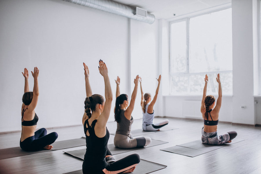 A group of women in a yoga studio sitting on the floor with their hands in the air