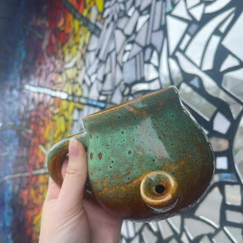 functional pottery style mug with smoking capabilities being held in front of a colorful glass mosaic 