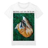 image of a white tee shirt on a white background. tee has full body print that says in black on top, being as an ocean with a photo of a sleeping fox on green grass. 
