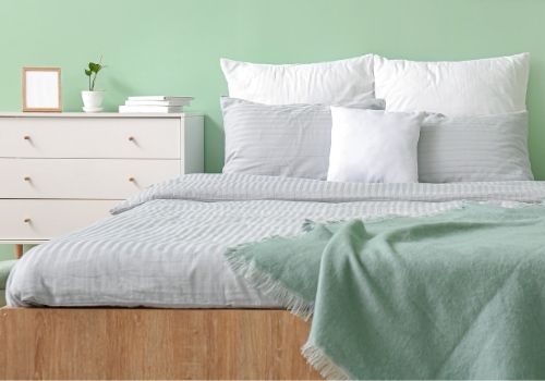 Bedroom painted in a soft mint green with white and grey accent pillows and duvet. A portrait of a room decorated in Spa Day inspired colours.