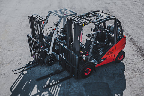 Two forklifts side by side in a warehouse parking lot