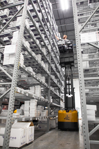 A mobile Joey picking cart lifts a warehouse employee to top shelves to pick inventory for outgoing orders