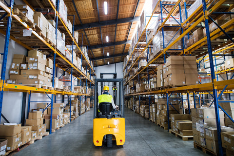 Warehouse worker driving forklift between rows of pallet racking