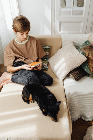 A boy sits on a couch with his dog 