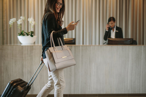 Woman using mobile phone and pulling her suitcase in a hotel lobby.