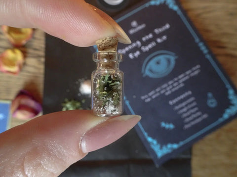 Mini glass bottle with herbs being held between thumb and index finger