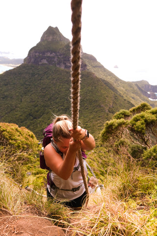 Sadie climbing a rope with mountain in background