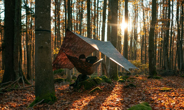 a man relaxing in a camouflage hammock with a tarp