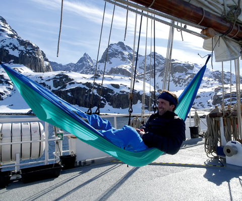 man sat in a blue hammock in a snowy mountain landscape