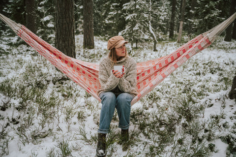 woman sat with a drink in a hammock enjoying a snowy day