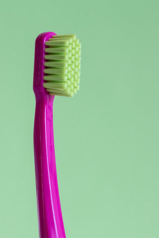 Dark pink traditional toothbrush with green nylon bristles in front of green background, for AutoBrush blog