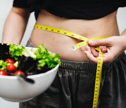 Person holding bowl of salad with measure tape around waist, for AutoBrush blog