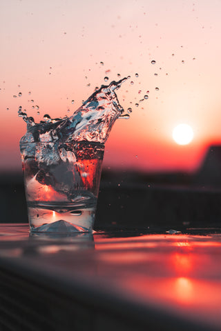 Glass of splashing water with a sunset in the background, for Autobrush