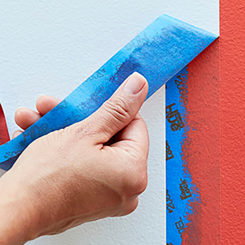 Peeling off blue 3M painter's tape from a wall.