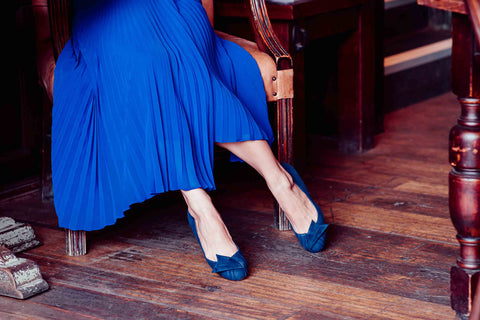 woman in cafe in blue pleated skirt and blue suede shoes