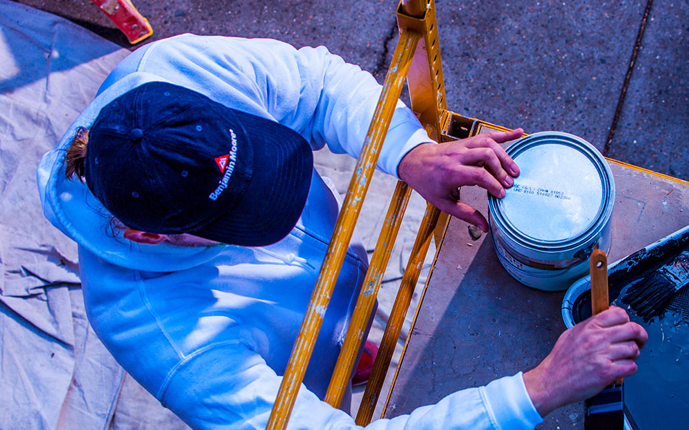 A drop cloth with a navy blue baseball cap with the Benjamin Moore logo, with a Benjamin Moore paint brush.