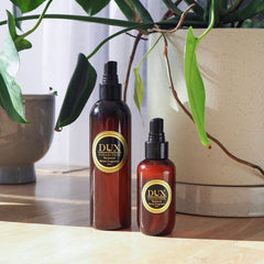 Two Essential Oil Room Sprays on a wooden table with two pot plants