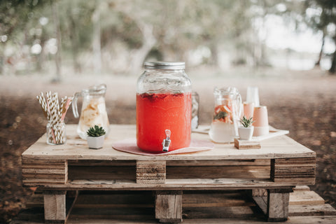 Juice dispenser, jugs, cups and straws on rustic wooden table