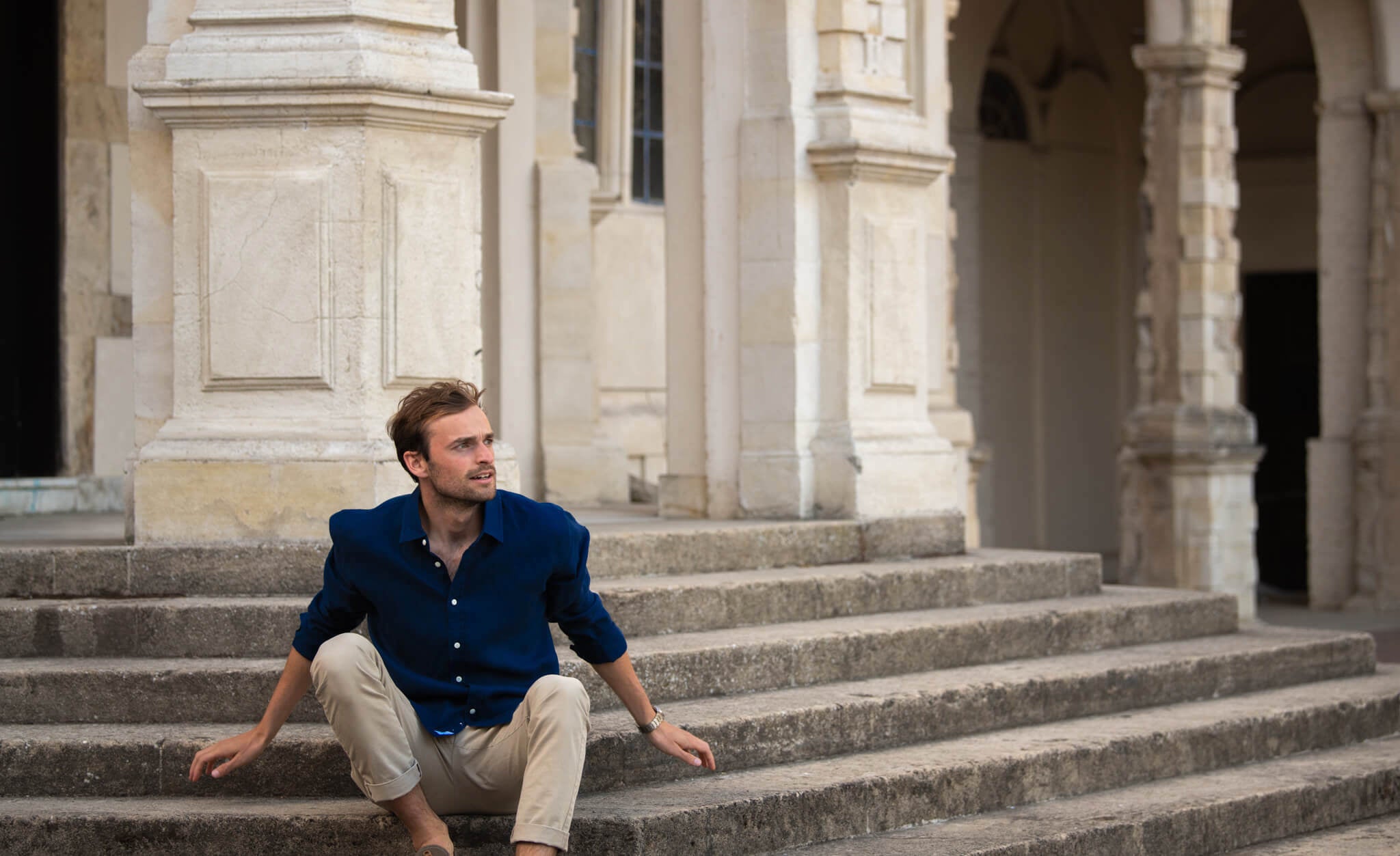 Harry, our model, sitting on steps whilst modelling a navy blue hemp shirt. hemp clothing by babble & hemp. location is London. the fabric of the shirt is 100% hemp.