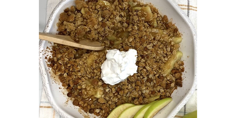 Final Product - Apple Crisp with whipped cream and garnished with additional fresh green apples. Wooden serving spoon is cutting into the final product.
