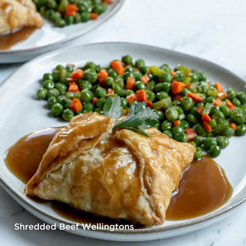 Shredded Beef Wellingtons. Image depicts a singular shredded beef wellington with a demi-glaze sauce poured on top. A side of peas and carrots sits behind the wellington on a white plate.
