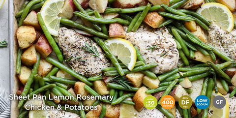 A birds eye view of the Sheet Pan Lemon Rosemary Chicken and Potatoes Meal. The baking sheet pan contains seasoned chicken breasts, baby potatoes, green beans and lemon slices. Image shows the meal icons in the corner: Under 30 minutes, dairy-free, under 400 calories, low sodium and gluten-free.