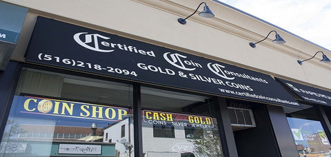 Certified Coin Consultant's Storefront location in Rockville Centre, NY. It features a black banner with the company name, phone number, and website in white letters. There is a neon "open" sign and a "Coins Gold" Sign.