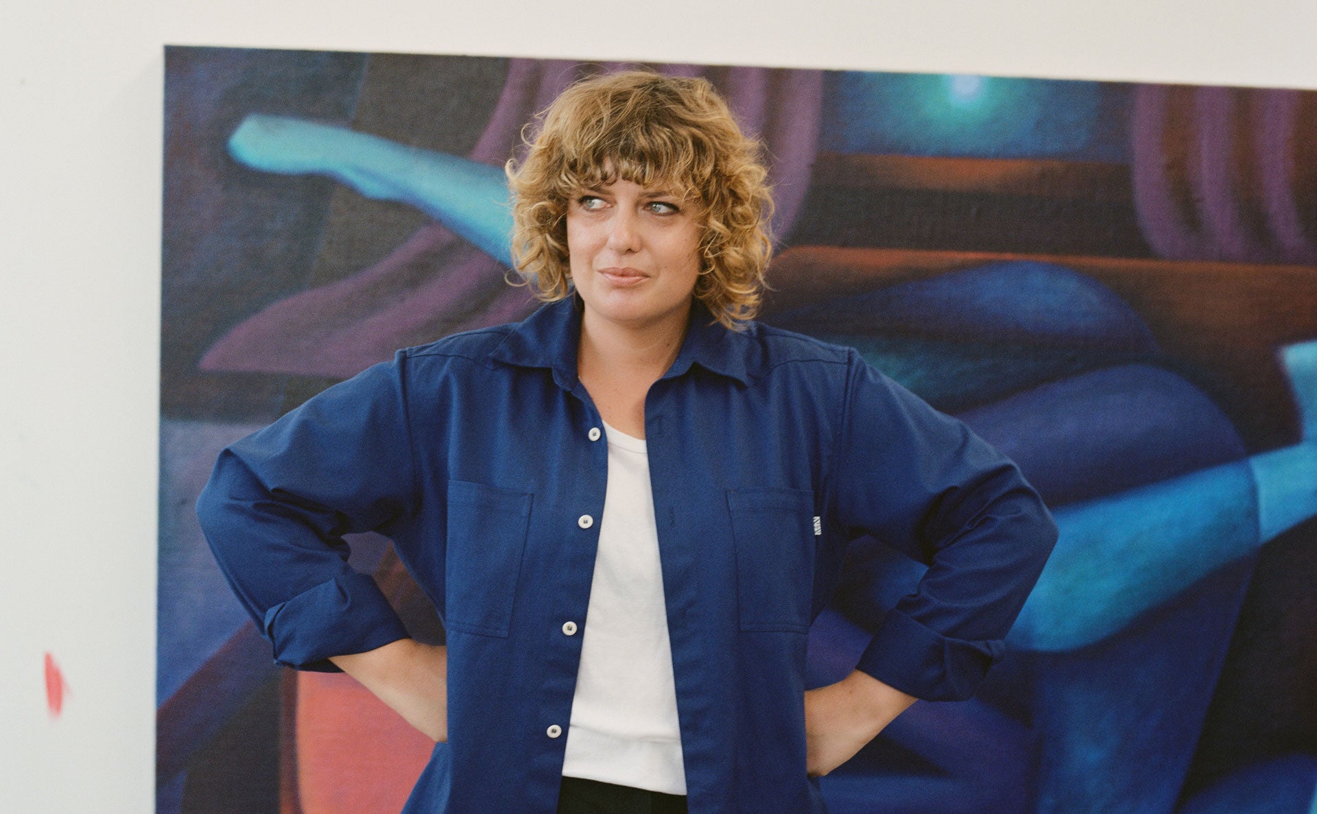 Imogen taylor wearing an M.N Uniform navy blue shirt standing in front of a large painting