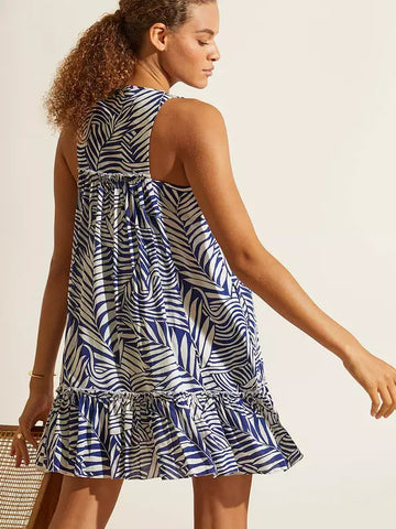 Woman with her back turned in profile, wearing a short white and blue dress with palm leaves as a pattern