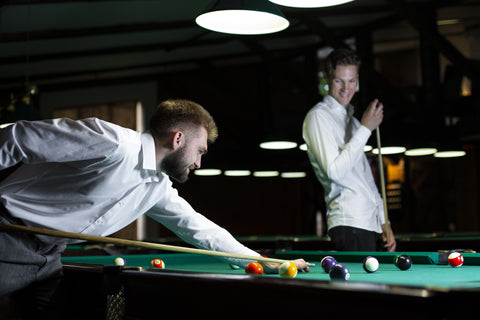 two adult friends playing billiard snooker with two cue sticks on a pool table