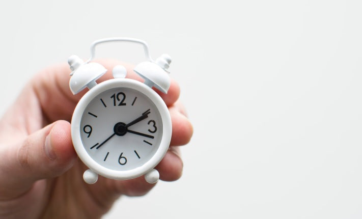 Person holding a small white alarm clock