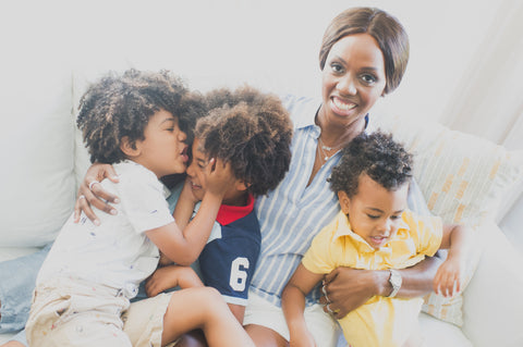 black woman sitting on the couching trying to hold her three young sons for a photo