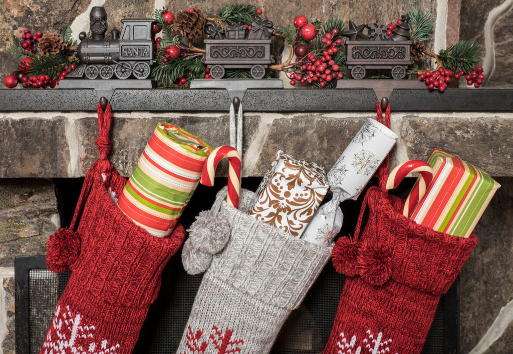 Three Christmas stockings with gifts in them hung by a fireplace