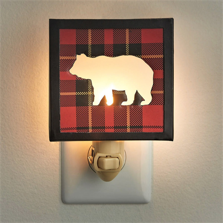 White bear shows through the red plaid and black framed night light. The cream-colored switch is seen below. It is plugged into a white plate all on a a textured cream-colored background.