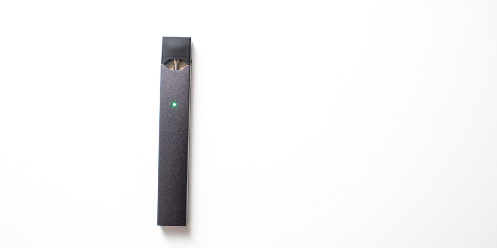 A black, all in one disposable vape with a green light filled with extract laying over a white background