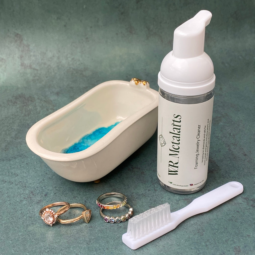 Jewelry Cleaning Kit, four rings, and a mini porcelain bathtub on teal background
