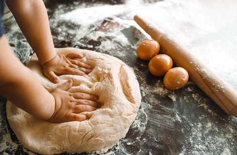 Kid pounds and kneads dough in the kitchen