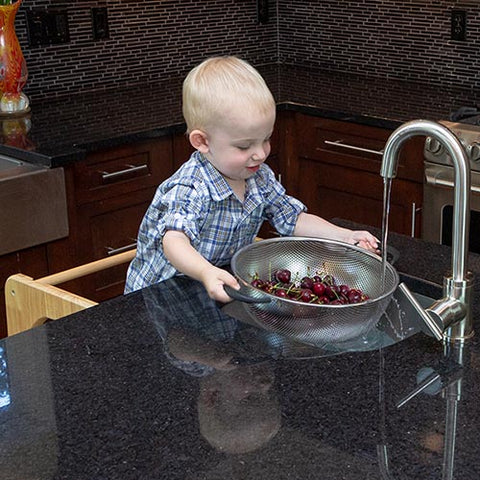 Toddler washing fruit in the kitchen